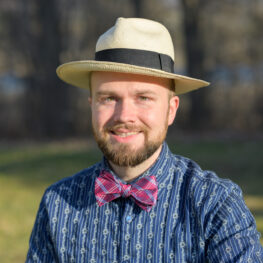Keli Fancher is smiling directly at us, wearing his signature straw hat with black band, and a particularly jaunty fuchsia and blue bow tie. His blue shirt has pinstripes of printed daisy chains and his green eyes and bearded smile somehow convey that he is a really fun dad!