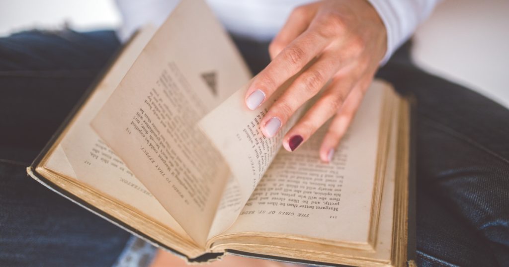 Open book held by a person with painted nails, about to flip a page.