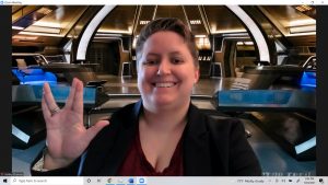 Ashley was born in Tennesseee but works in space. Here she is greeting us from the bridge of the Discovery, where she will interview the crew for her ongoing work as Coolest Social Media Journalist in Star Trek universe. she's greeting you with the Vulcan salute for long life and prosperity, and her grin is absolutely infectious.