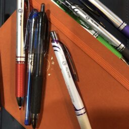 a jumble of colorful pens scattered joyfully across an orange-covered journal.