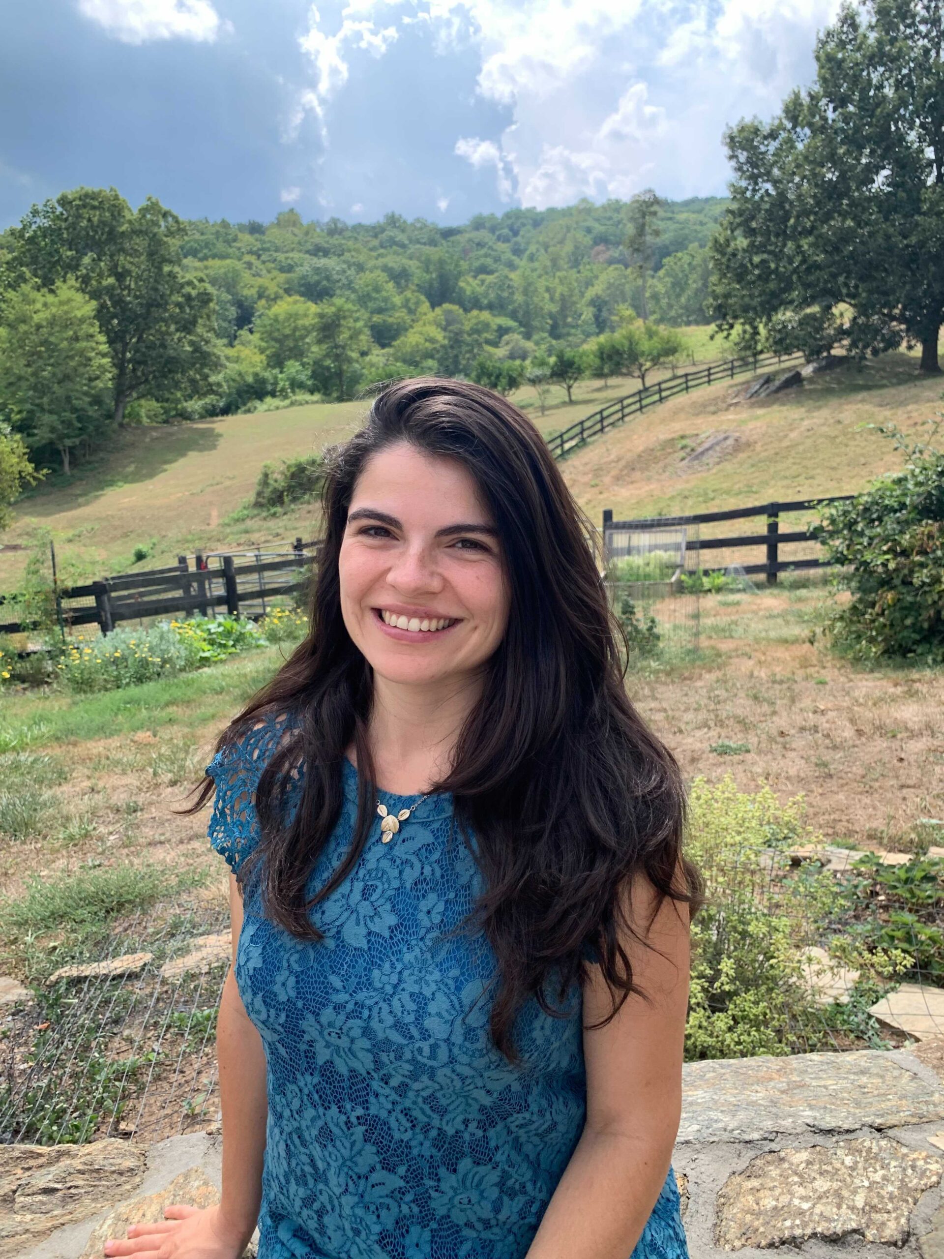 Jennifer Rogers is outstanding in her field — literally — with a split rail fence in the background and deciduous woods beyond that. This scholar of European and Hispanic ancestry has a wide, welcoming smile which is reflected in her eyes. She has chosen a rich blue top and wears her dark hair flowing freely.