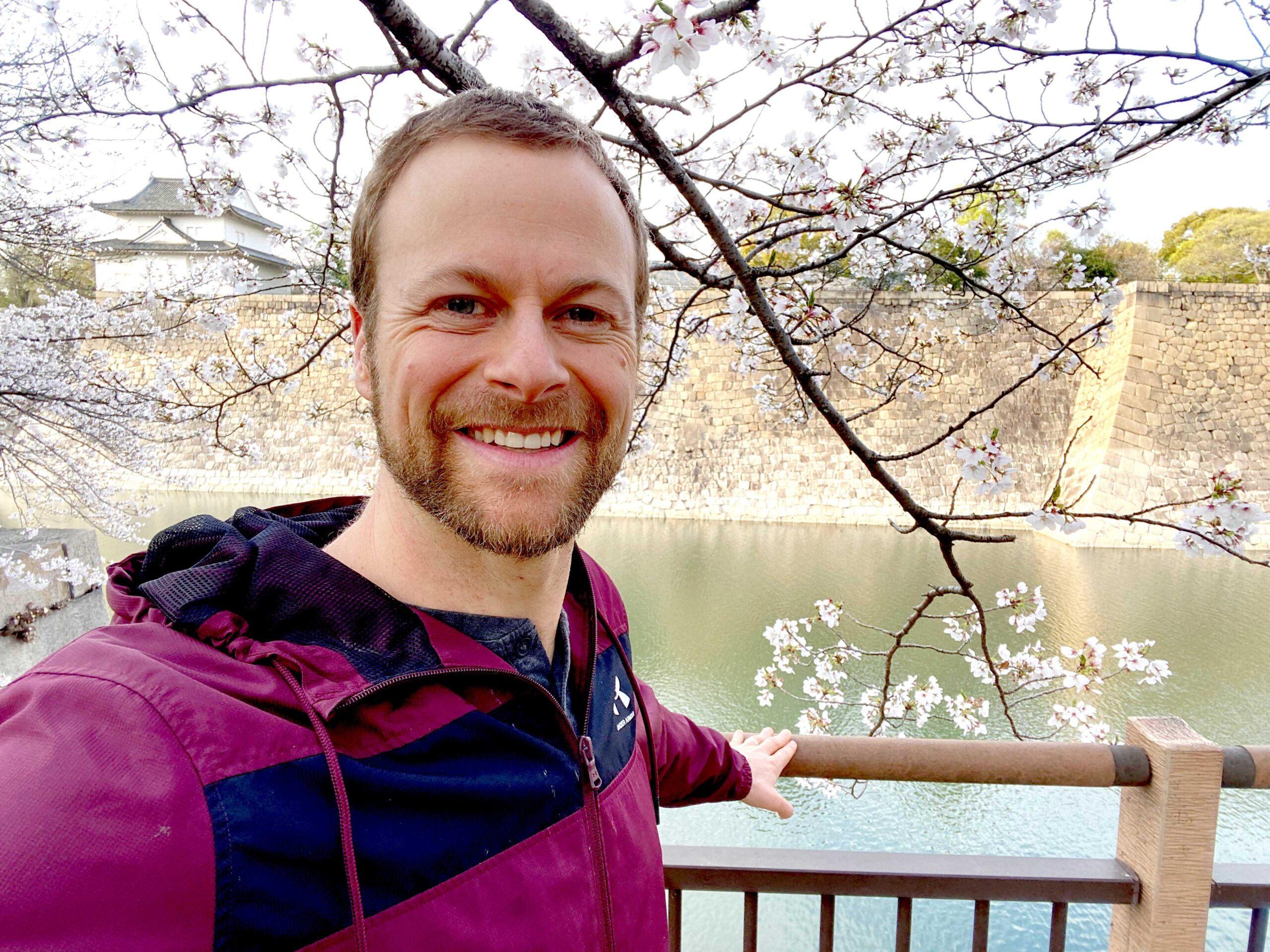 Rob is bearded now! This photo in a cheerfully colored jacket shows a scene from his fabulous trip to japan with beautiful blossoming trees, a peaceful bit of water, and a broad welcoming smile.