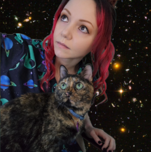 A red-haired woman of Euriopean descent and a brindled cat of mysterious provenance with startling green eyes both gaze upward. A background of stars and galaxies supports their out-of-this-world attitude!