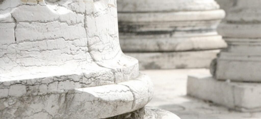 The bases of three cracked and scarred white stone columns