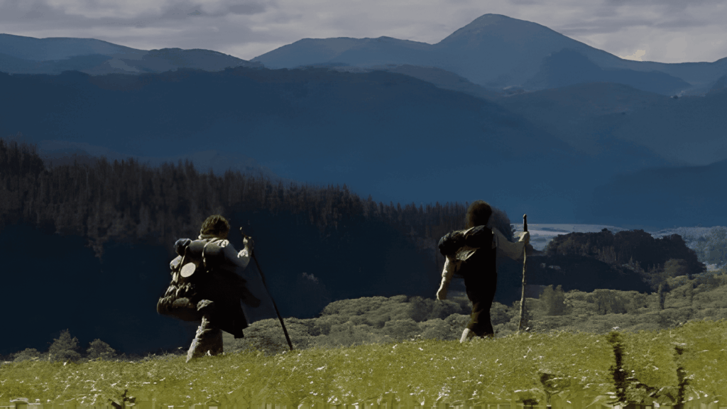 Frodo and Samwise from The Lord of the Rings walking through the meadows of the Shire with rucksacks and walking sticks.