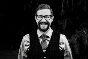A bearded and bespectacled gent with a broad smile and a particuolarly jaunty dotted necktie