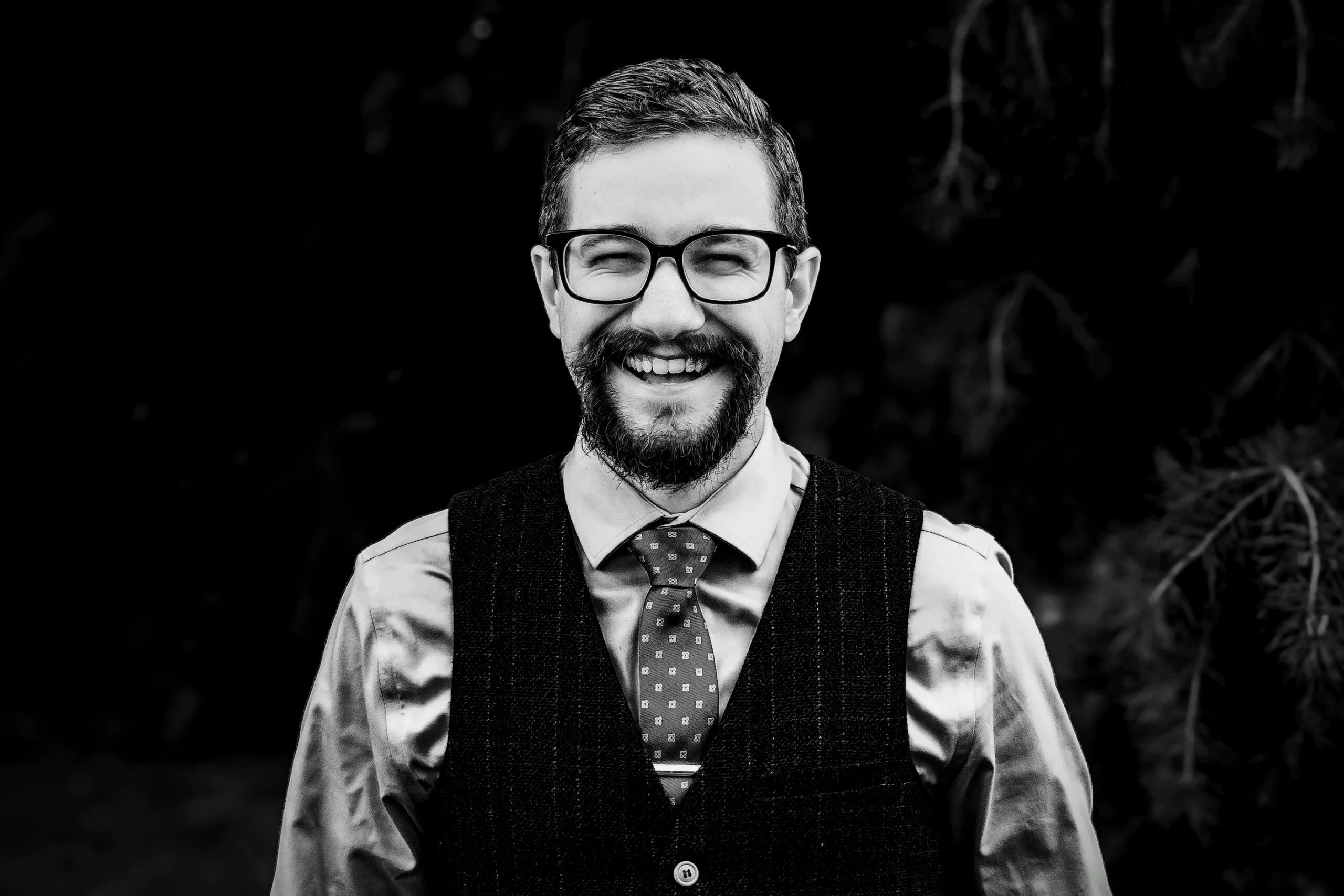 A bearded and bespectacled gent with a broad smile and a particuolarly jaunty dotted necktie